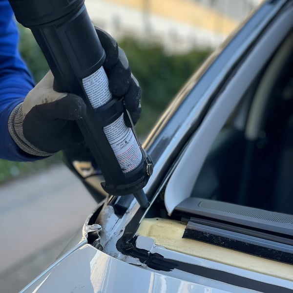 Fachkraft trägt Scheibenkleber auf die Fahrzeugkante zur Reparatur auf