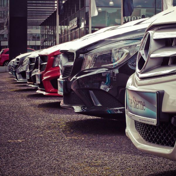 Reihe geparkter Fahrzeuge vor einem Autohaus, Fokus auf Fahrzeugfronten mit Mercedes-Stern