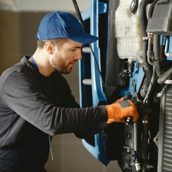 Mechaniker mit Handschuhen arbeitet an einem geöffneten LKW-Motor in einer Werkstatt